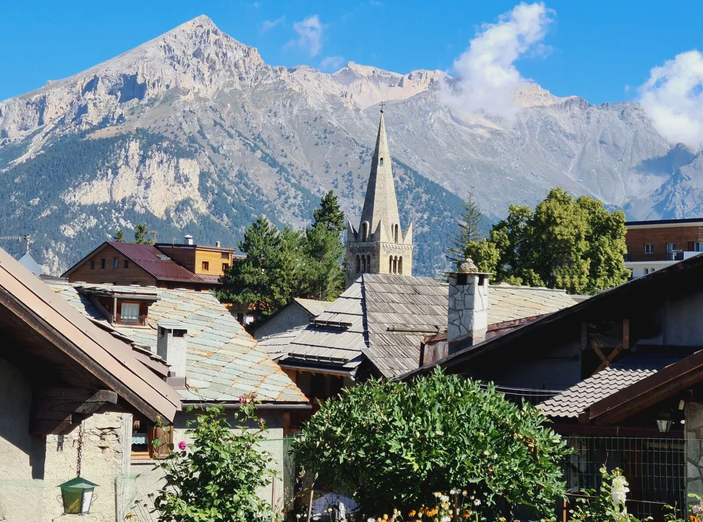 Vue pittoresque du village de La Grave avec le clocher de l’église Notre-Dame-de-l’Assomption au centre, encadré par les toits de pierre et les montagnes majestueuses des Alpes françaises.