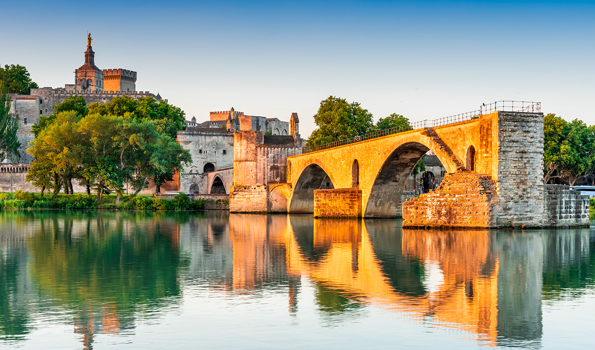 Pont d’Avignon et Palais des Papes se reflétant dans le Rhône au coucher du soleil.