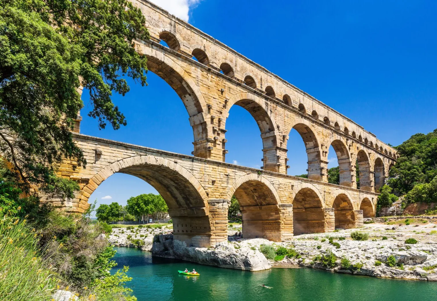 Pont du Gard, ancien aqueduc romain à trois niveaux enjambant la rivière Gardon, entouré de nature et de ciel bleu.
