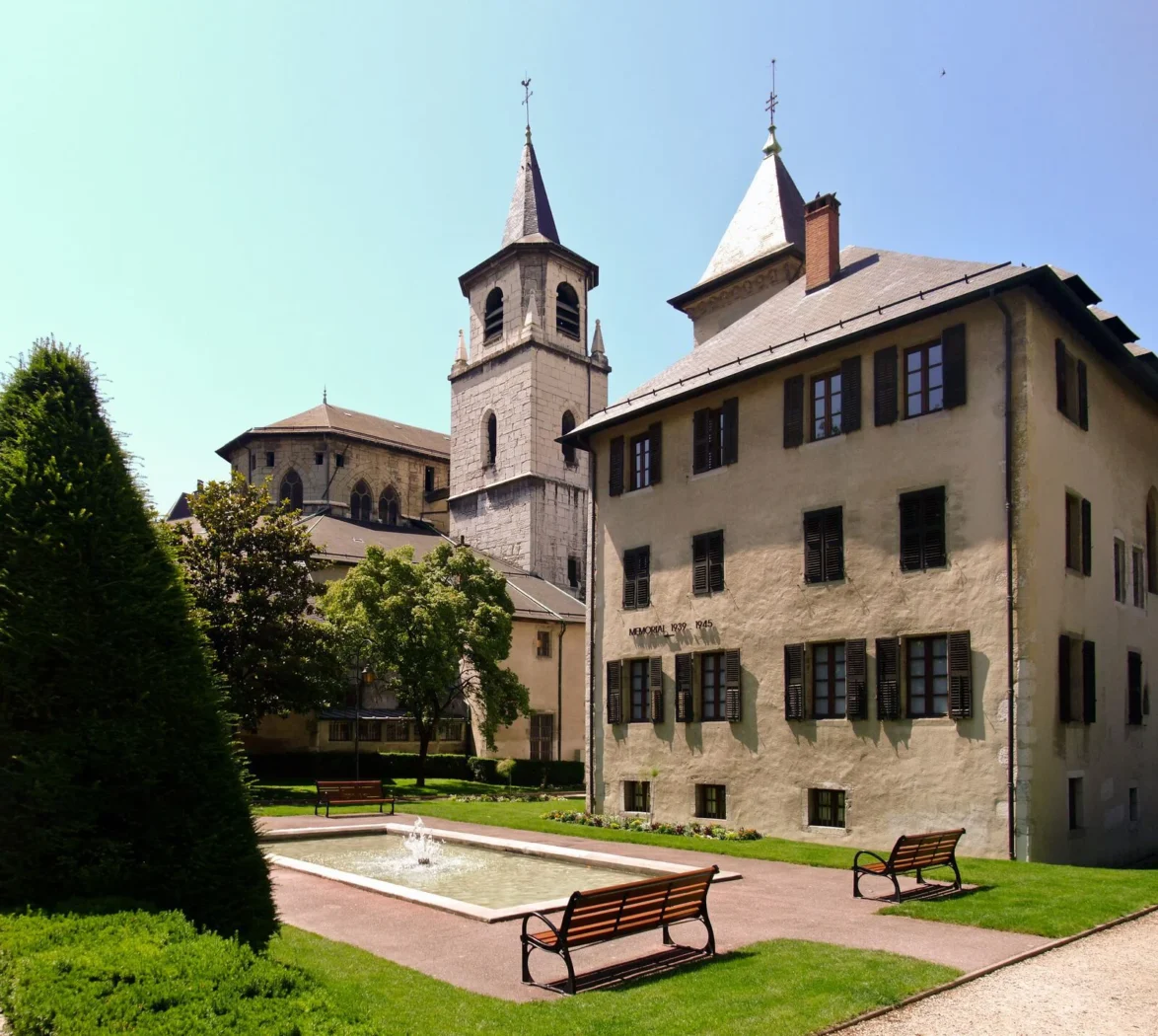 Vue sur la cathédrale Saint-Pierre d’Annecy et les jardins paisibles environnants avec bancs et bassin.
