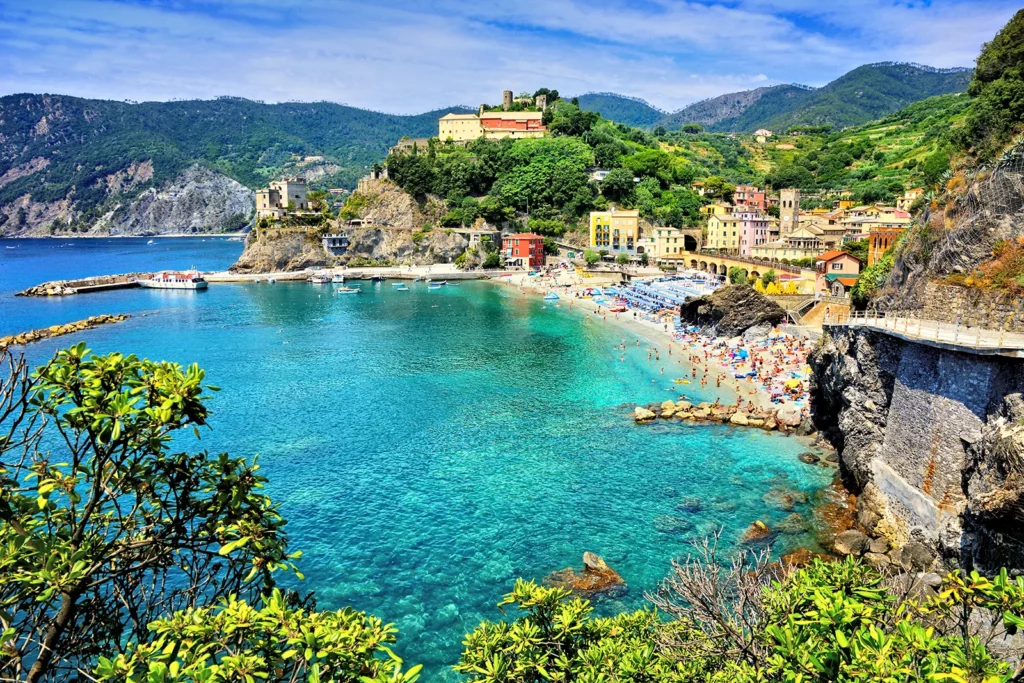 Vue panoramique sur Monterosso al Mare, village coloré des Cinque Terre, avec plage, collines vertes et mer turquoise.