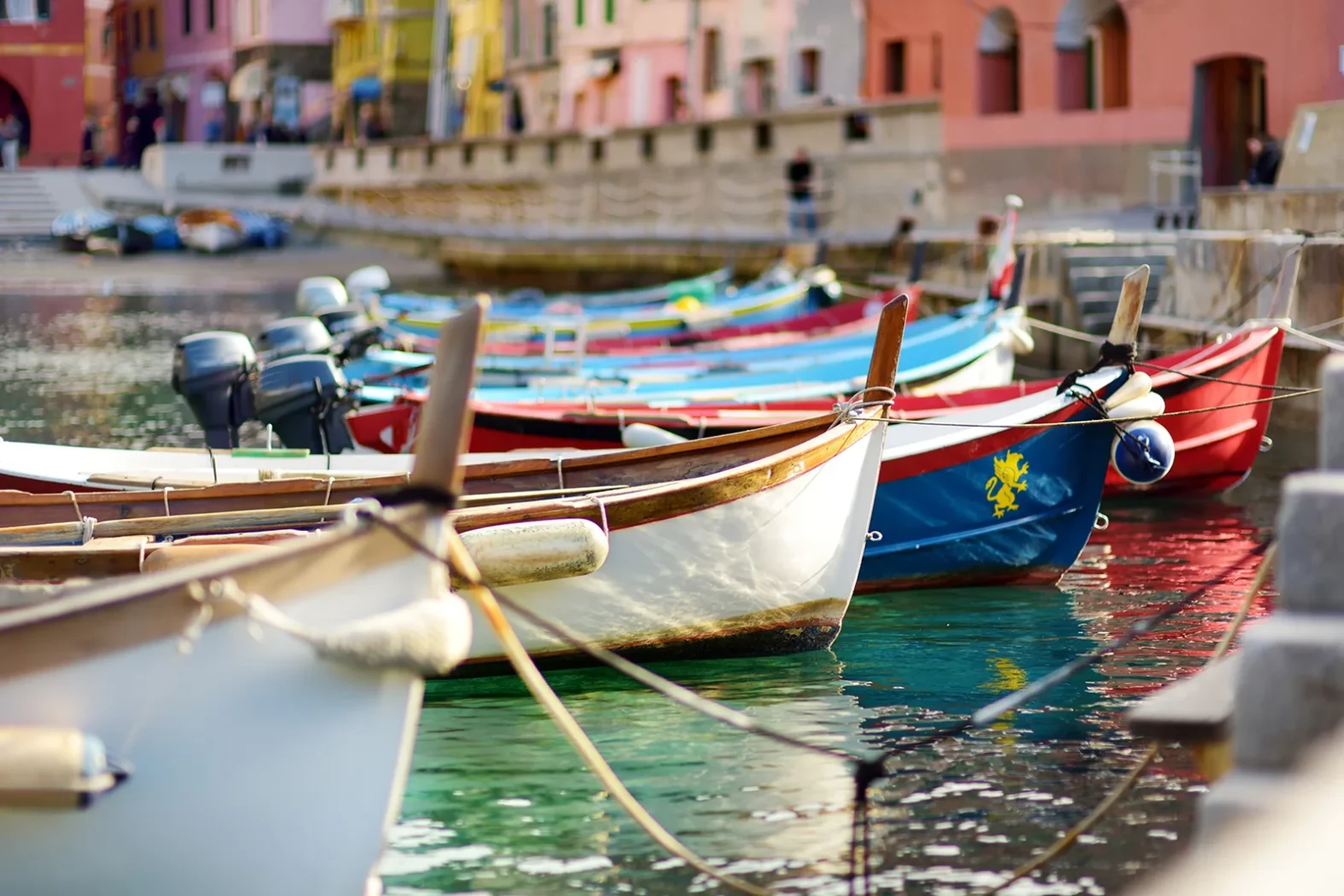 Rangée de barques colorées amarrées dans le petit port de Vernazza, avec reflets sur l’eau turquoise.