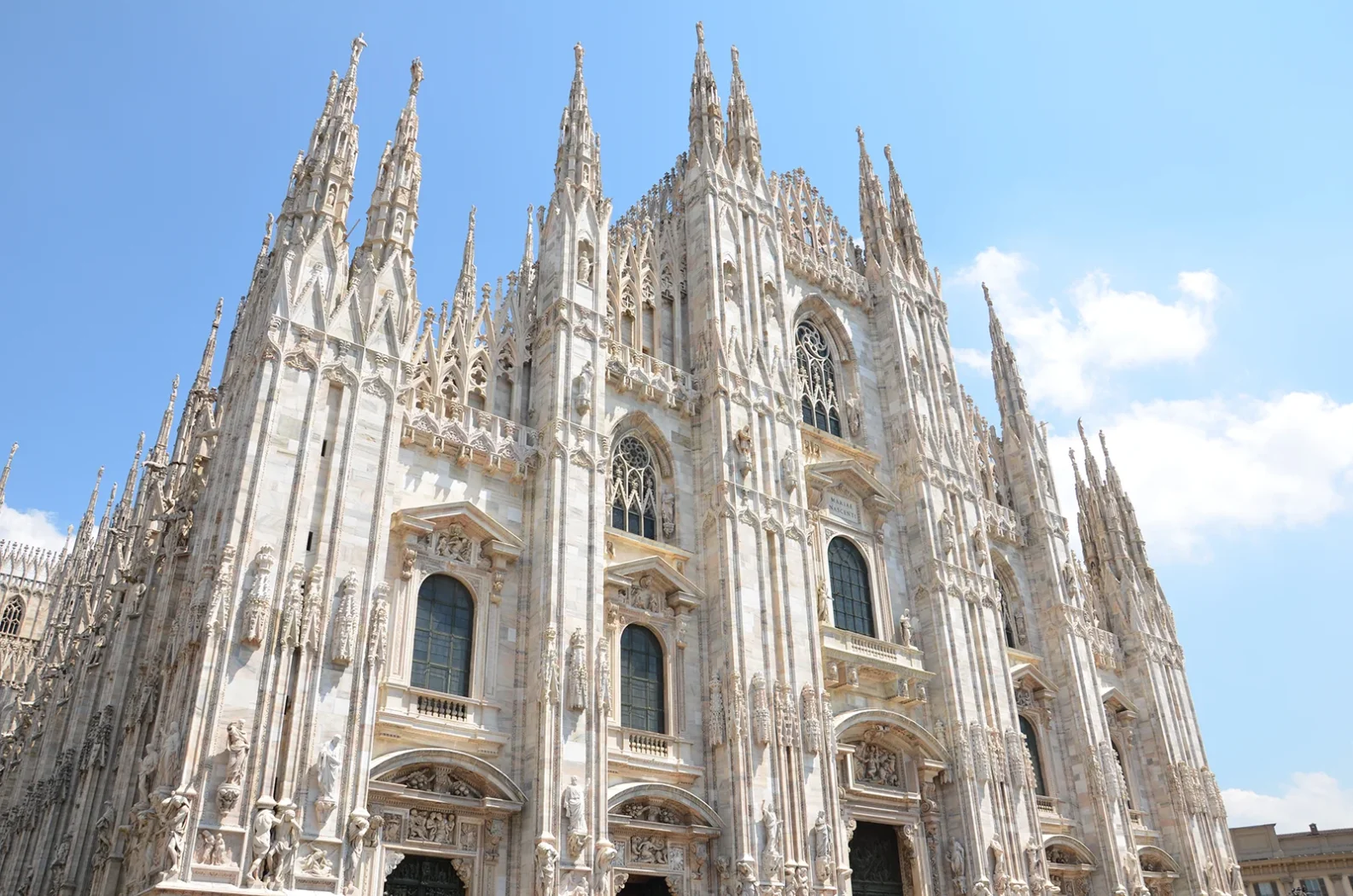 Façade gothique du Duomo de Milan en marbre blanc sous un ciel bleu.