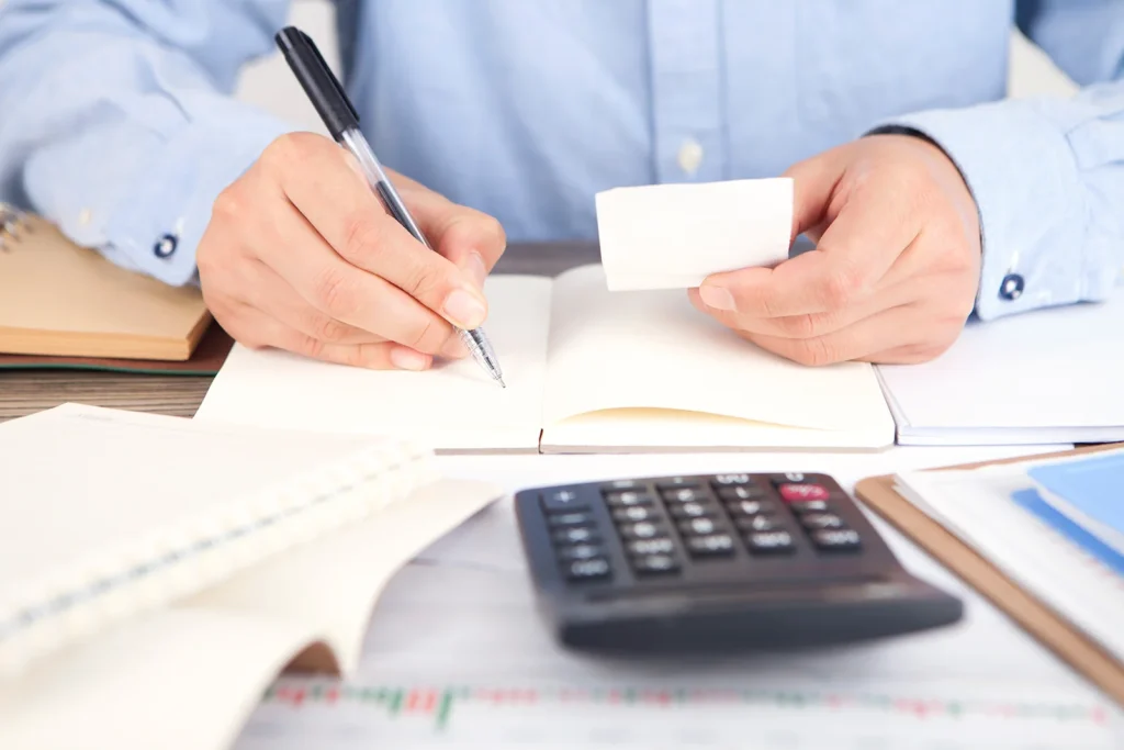 Main écrivant dans un carnet avec une calculatrice.