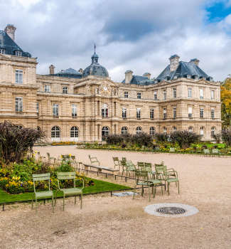 Palais historique entouré d’un jardin avec des chaises vertes et des parterres fleuris.