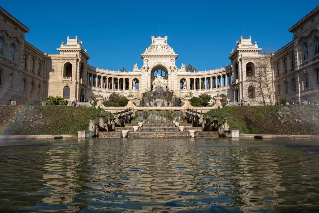 Palais Longchamp à Marseille avec sa fontaine monumentale et son bassin sous un ciel bleu.