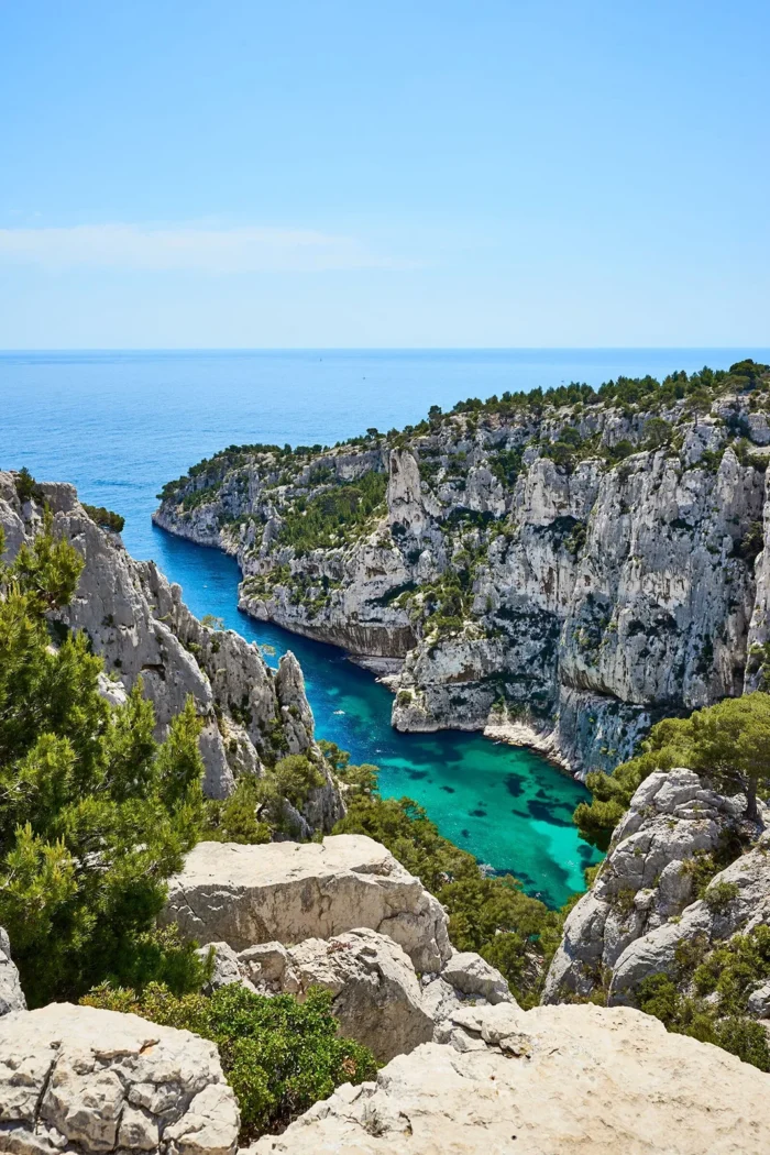 Vue aérienne d’une calanque à Marseille avec falaises blanches, pins et eau turquoise sous un ciel dégagé.