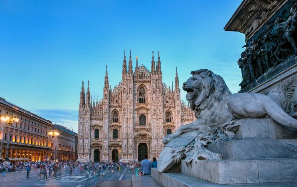 Façade du Duomo de Milan au crépuscule avec la statue du lion sur la place.