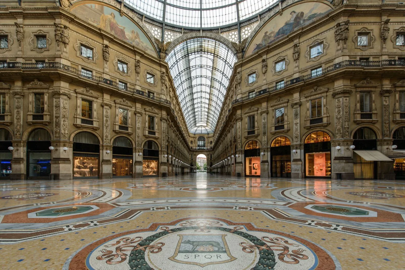 Intérieur majestueux de la Galerie Vittorio Emanuele II à Milan, avec sa verrière monumentale, ses arcades élégantes et ses mosaïques au sol.