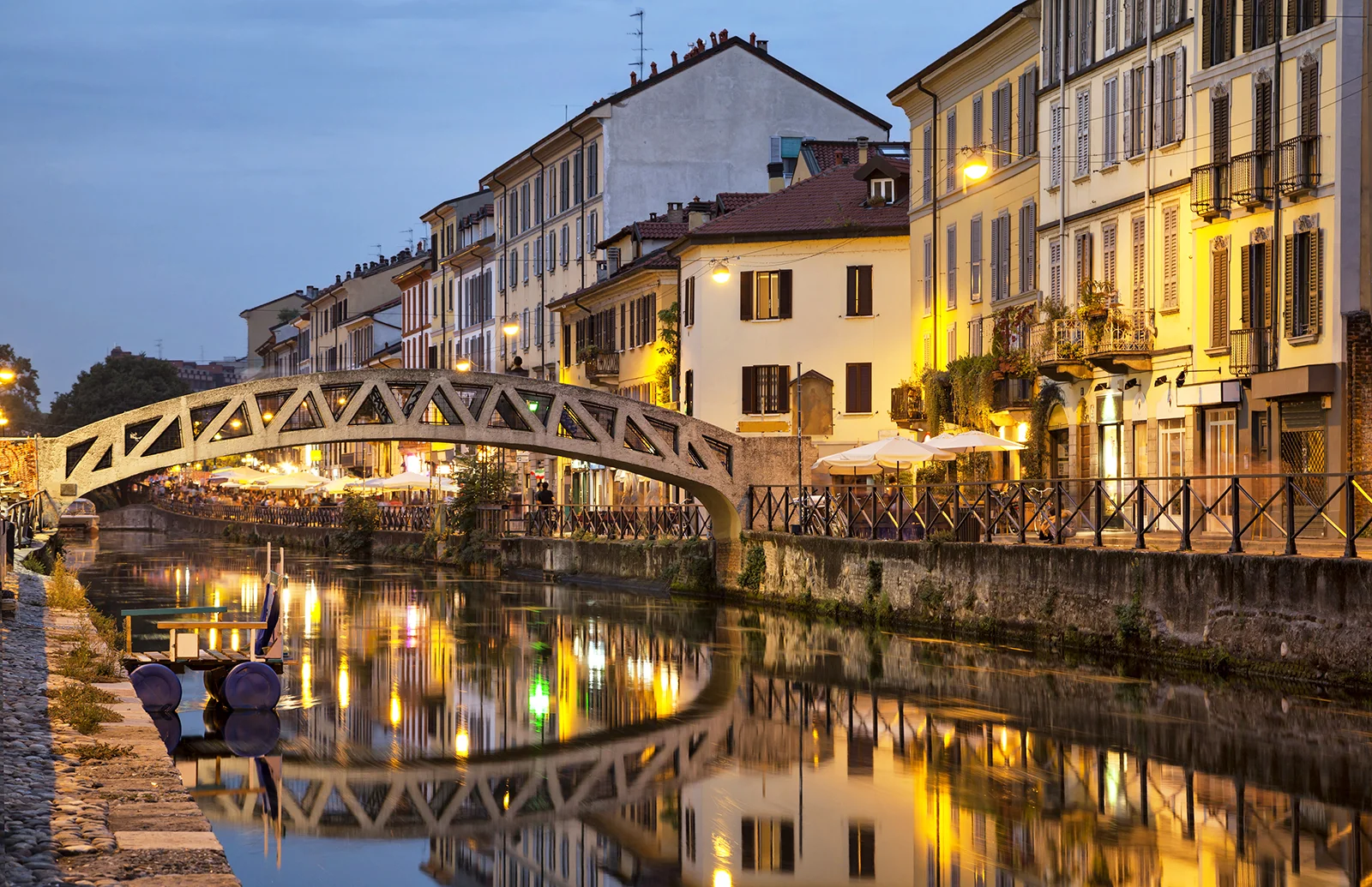 Pont en pierre au-dessus du canal Navigli entouré de bâtiments illuminés le soir.