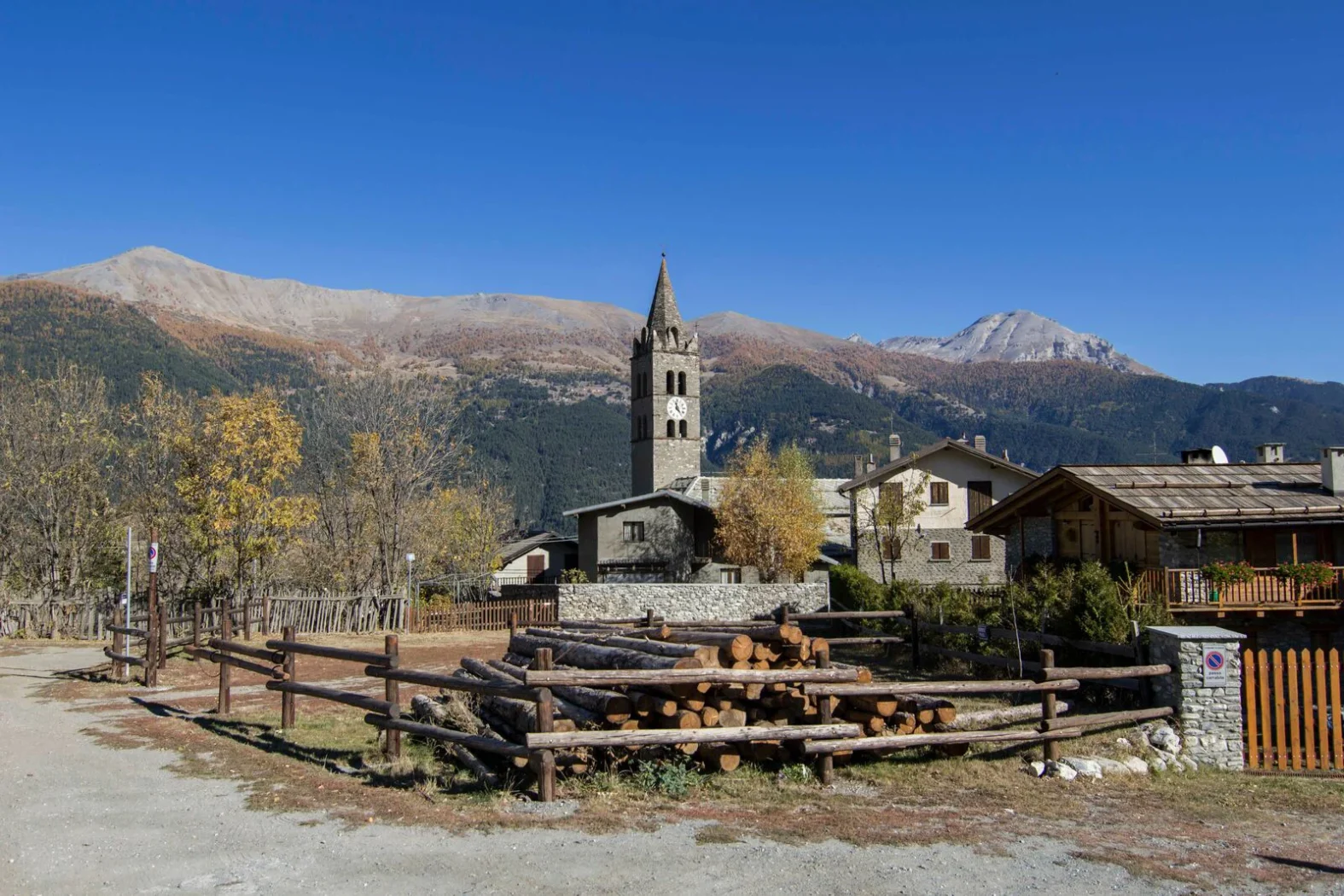 Vue rapprochée de l’église Notre-Dame-de-l’Assomption, son clocher roman et les chalets typiques des Alpes, sur fond de paysages montagneux.