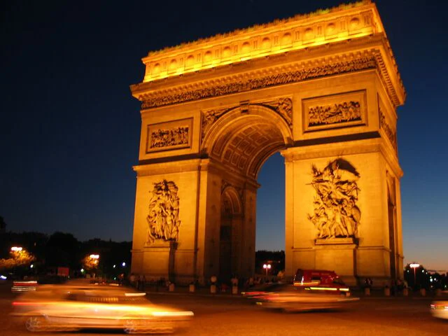 Arc de Triomphe illuminé la nuit sur la place Charles-de-Gaulle avec des voitures en mouvement.