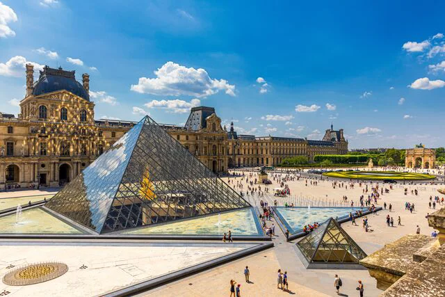 Vue sur la pyramide de verre du Louvre et la cour Napoléon sous un ciel bleu à Paris.