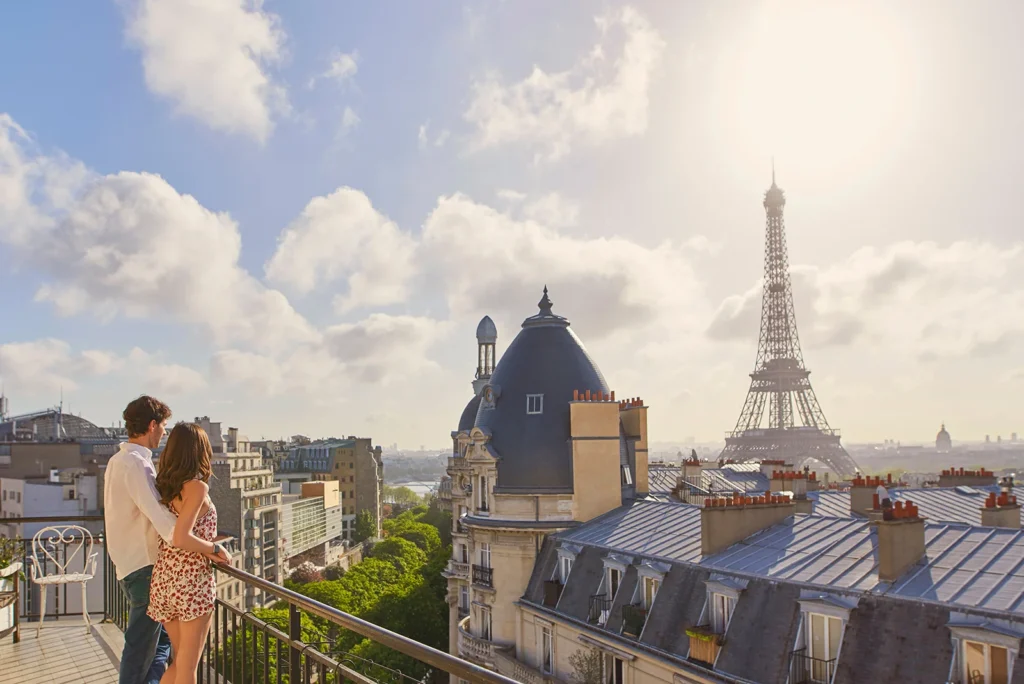 Couple admirant la Tour Eiffel depuis un balcon parisien au lever du soleil.