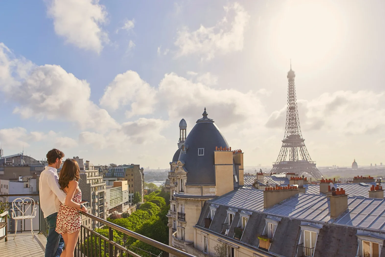 Couple admirant la Tour Eiffel depuis un balcon parisien au lever du soleil.