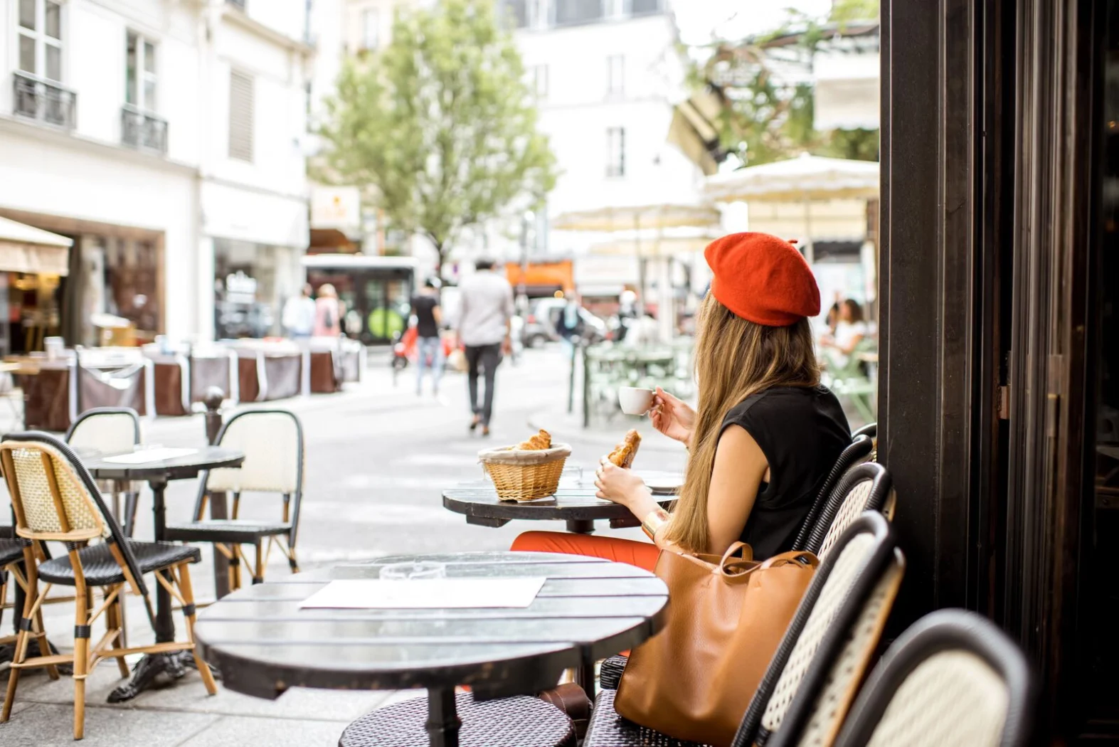 Femme portant un béret rouge prenant un café et un croissant en terrasse à Paris.