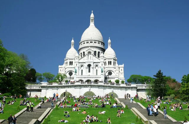 Basilique du Sacré-Cœur de Montmartre avec des visiteurs assis sur la pelouse.