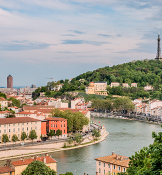 Vue d’une ville traversée par un fleuve avec des collines verdoyantes en arrière-plan.