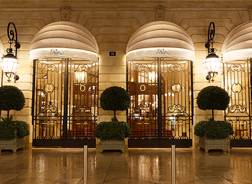 Façade élégante d’un hôtel illuminé avec grilles dorées et grandes lanternes.