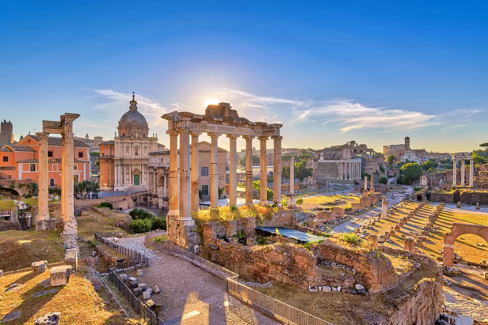 Ruines antiques du Forum romain à Rome baignées de lumière dorée, avec colonnes, temples et églises historiques.