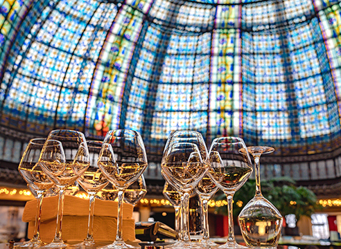 Verres à vin alignés sous une grande coupole en vitrail coloré.