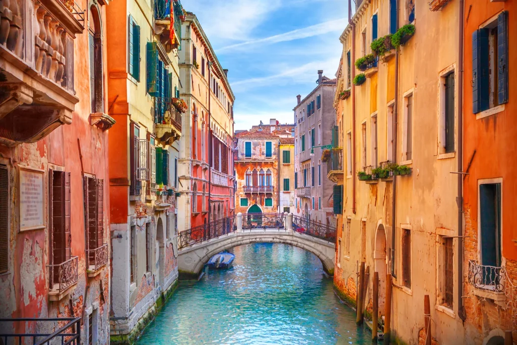 Canal étroit bordé de bâtiments colorés à Venise avec un petit pont en pierre et une barque amarrée.