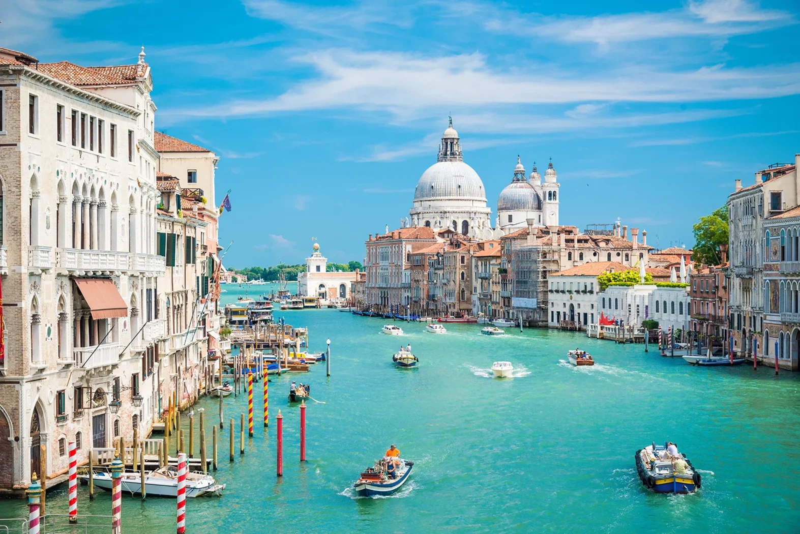 Canal de Venise avec des bateaux et la basilique Santa Maria della Salute sous un ciel bleu.