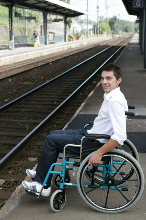 Homme en fauteuil roulant sur un quai de gare, attendant un train.