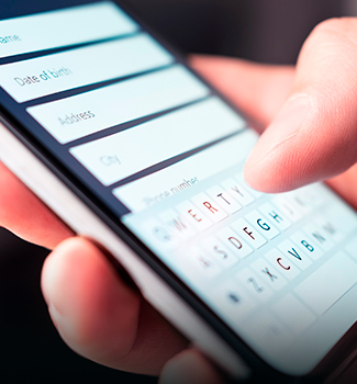 Gros plan d’une main saisissant des informations personnelles sur le clavier d’un smartphone, affichant un formulaire en ligne.