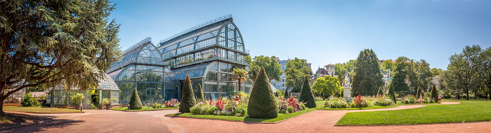 Vue panoramique du jardin botanique du parc de la Tête d’Or à Lyon, avec ses grandes serres vitrées et des allées fleuries.