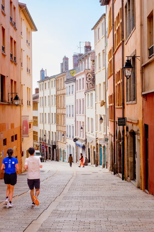 Rue colorée du Vieux Lyon avec passants et façades anciennes.