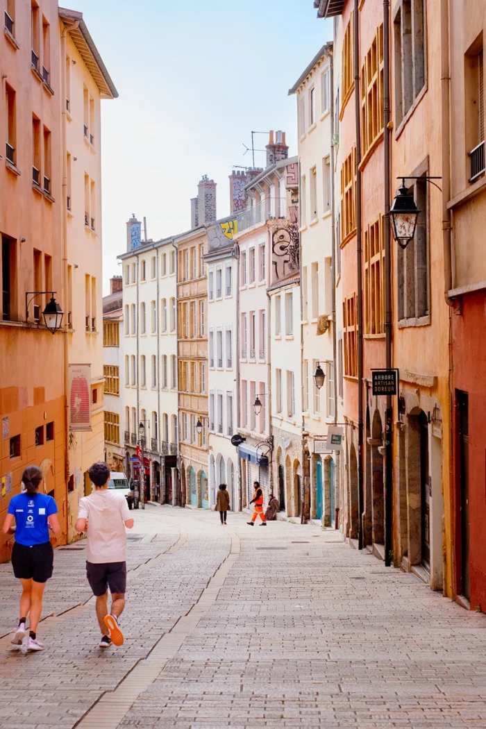 Rue colorée du Vieux Lyon avec passants et façades anciennes.