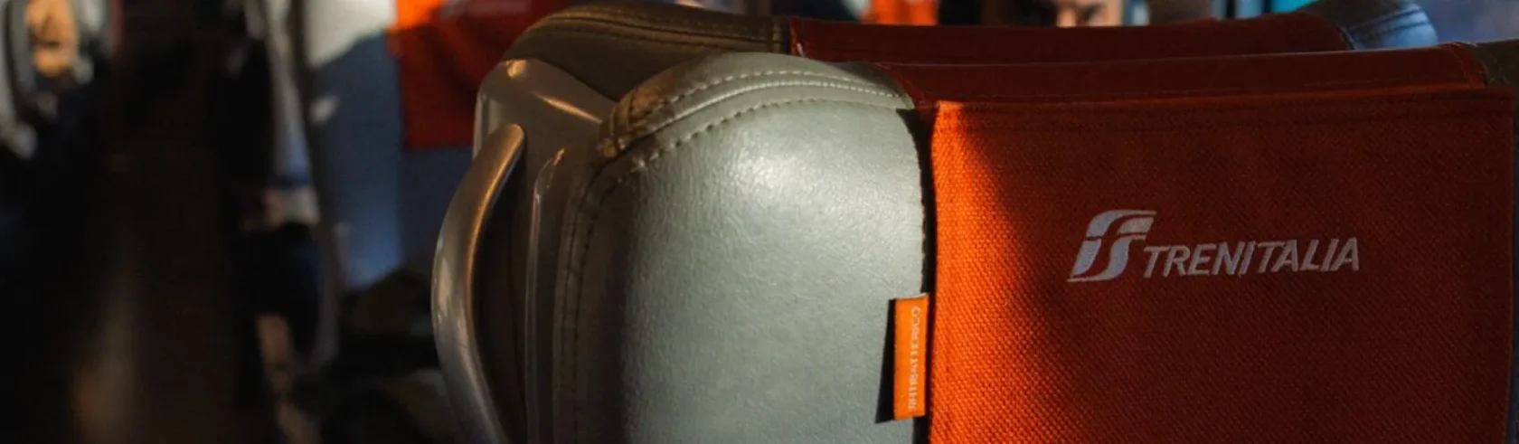 Siège en cuir gris avec appuie-tête rouge marqué Trenitalia dans un train italien.