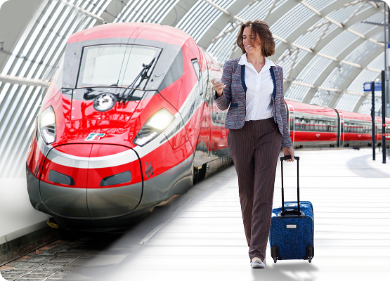 Femme d’affaires marchant sur le quai avec une valise devant un train à grande vitesse rouge de la compagnie Trenitalia, dans une gare moderne couverte.