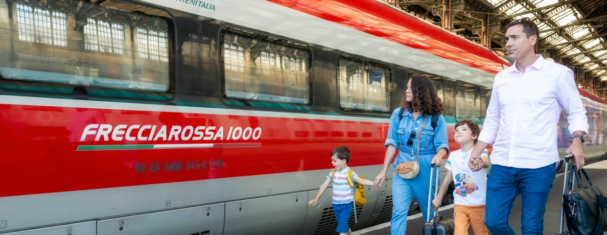 Famille avec deux enfants marchant sur le quai devant un train Frecciarossa 1000 de Trenitalia, valises à la main