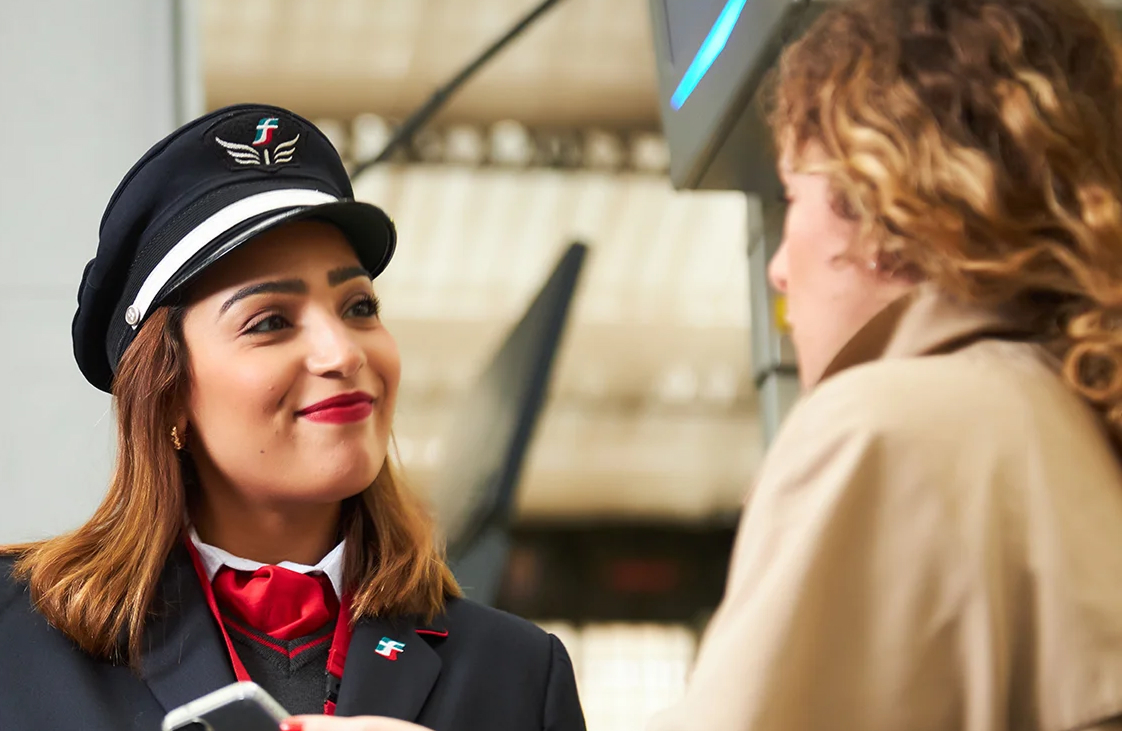 Une agente de train en uniforme discute avec une passagère pendant le contrôle d’un billet électronique.