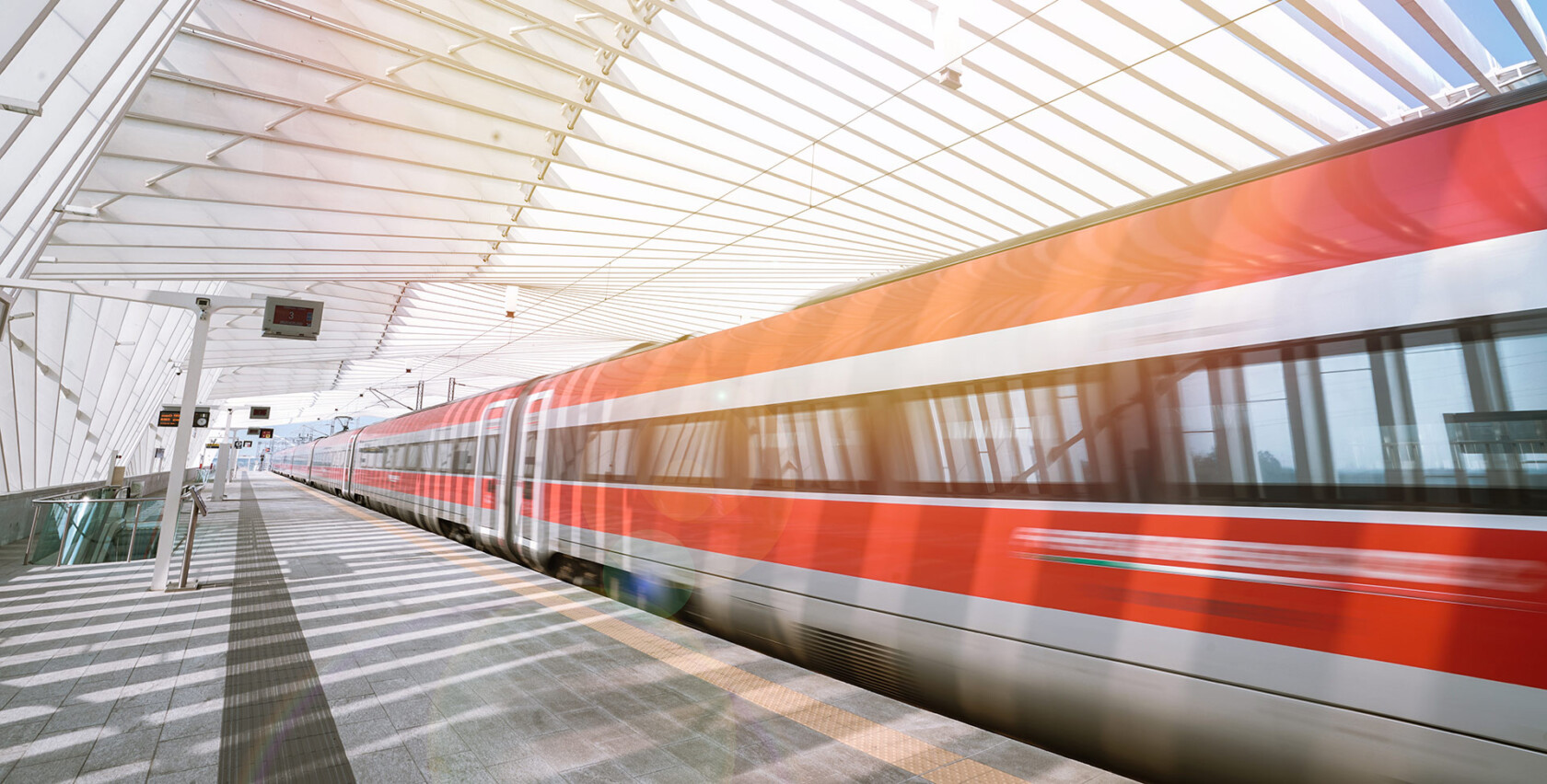 Train rouge et blanc à grande vitesse Frecciarossa entrant dans une gare moderne au toit vitré, baignée de lumière naturelle.