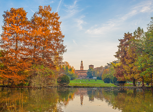 Vue automnale du parc Sempione avec le château des Sforza au loin, reflété dans un étang.