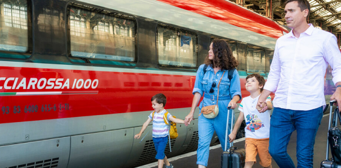 Famille avec deux enfants marchant sur le quai devant un train Frecciarossa 1000 de Trenitalia, valises à la main
