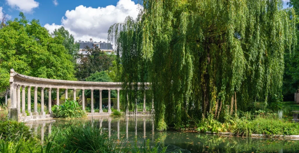 Colonnade et étang du parc Monceau à Paris sous un ciel bleu.