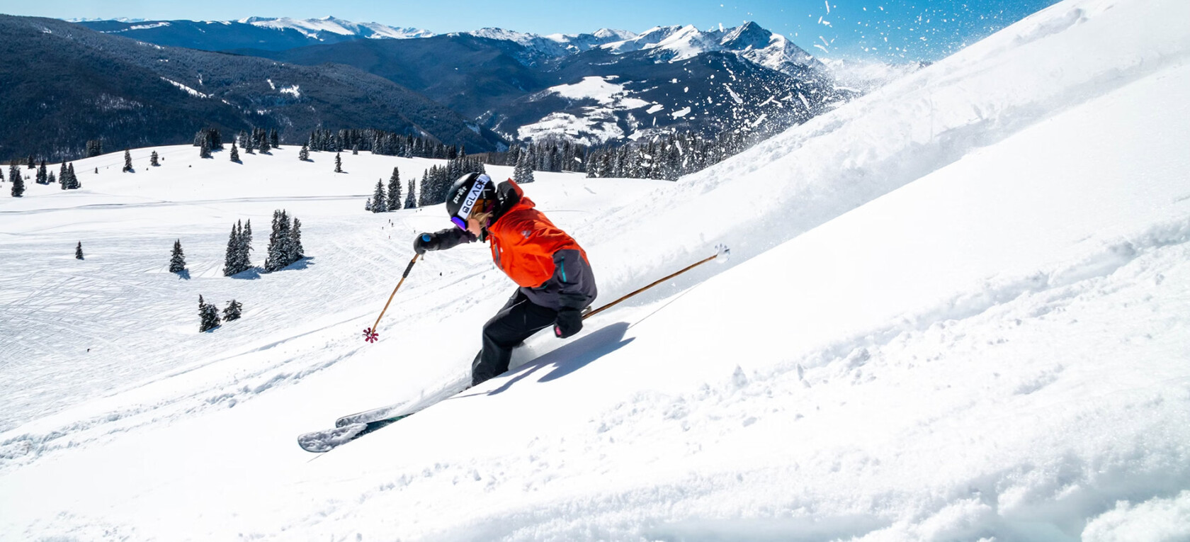 Skieur dévalant une piste enneigée dans les Alpes sous un ciel bleu.